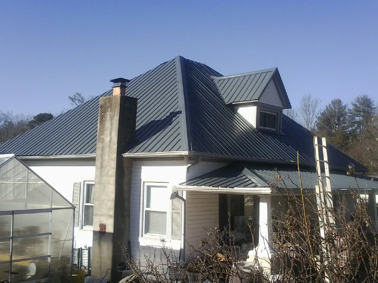 Dark blue standing seam metal roof on a white farmhouse with dormer — Slate & Tile Roof Repair by Roofing Brothers in Iowa Falls