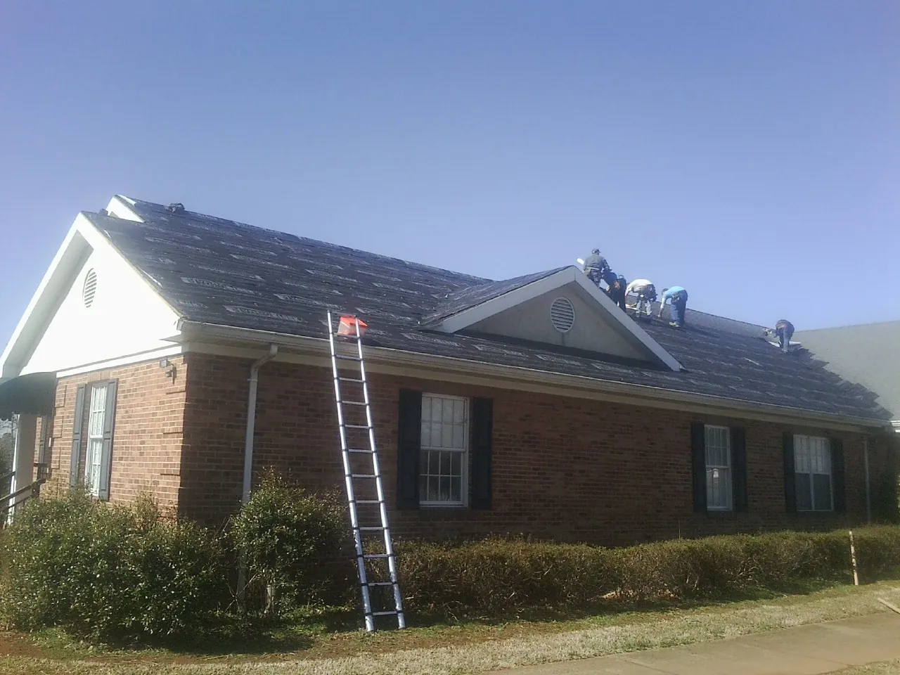 Crew tearing shingles off a brick ranch roof with a ladder set — Metal Roof Repair work by our crew in Iowa Falls