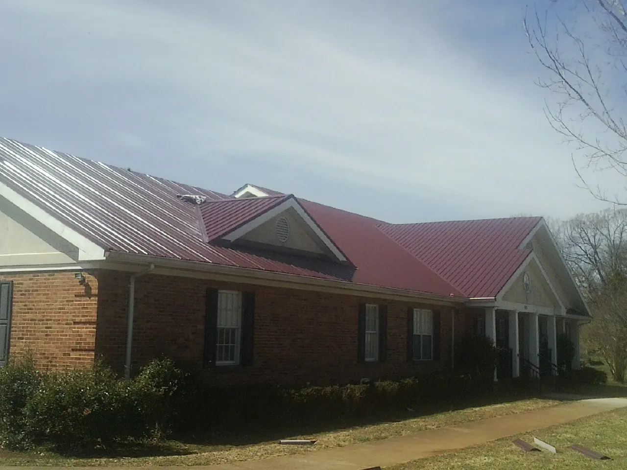 Red metal roof with gabled entries on a long brick building, from a Hail Damage Roof Repair job in Iowa Falls