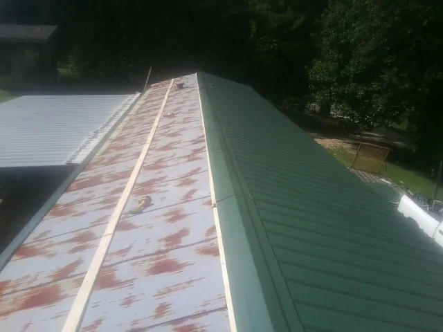 Old rusted panels beside newly installed green metal roofing — Wind Damage Roof Repair by Roofing Brothers in Iowa Falls