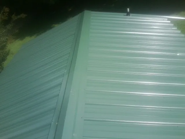 New green metal panels meeting at the ridge of a roof — Flat Roof Repair work by our crew in Iowa Falls