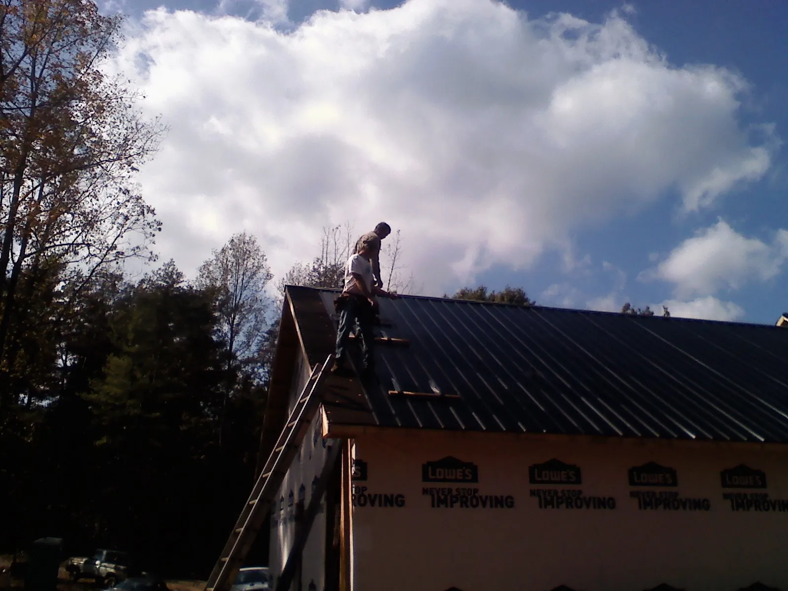 Roofer fastening dark metal panels high against a cloudy sky, from a Roof Inspection job in Iowa Falls