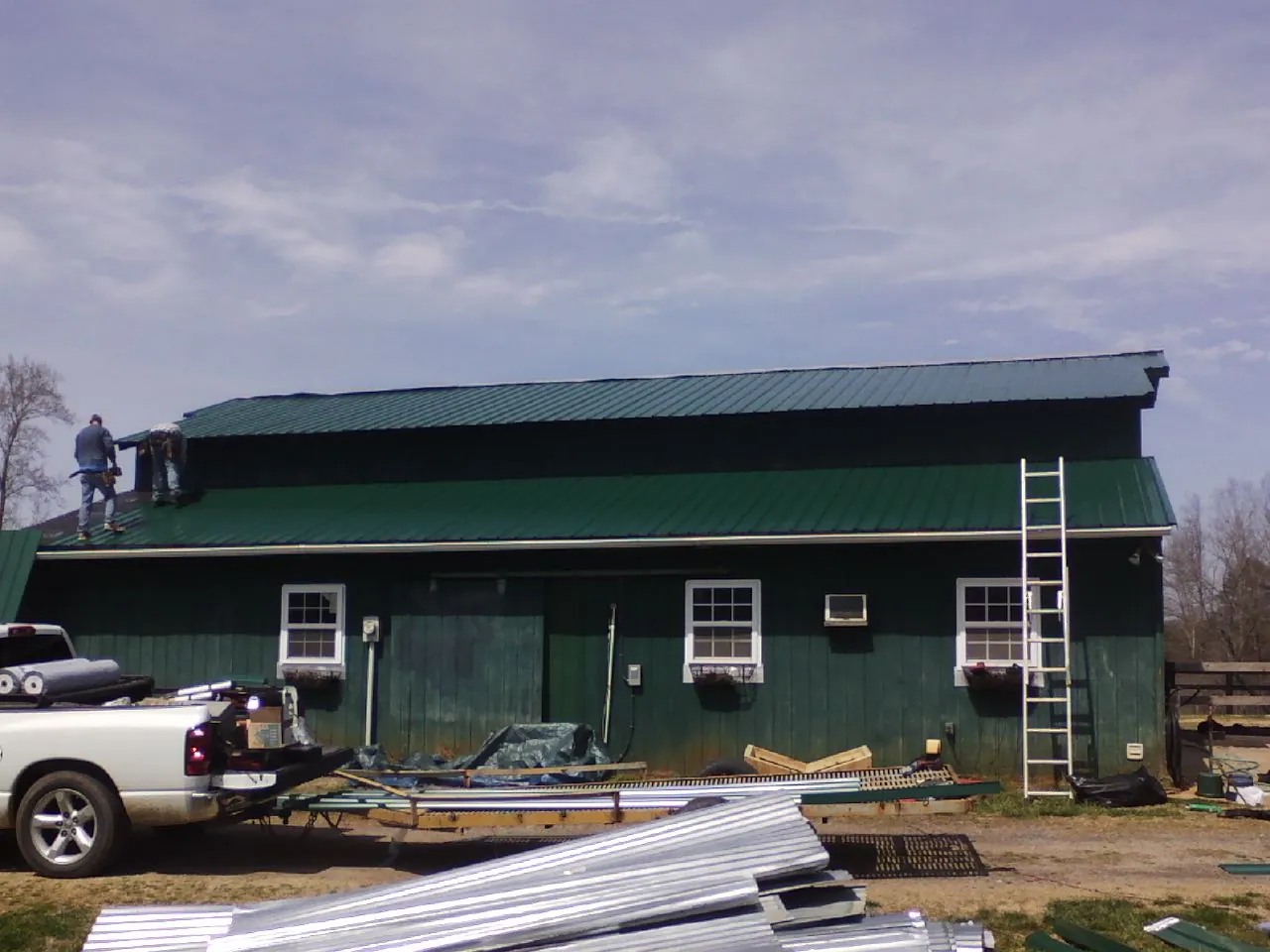 Crew installing green metal roofing on a large green barn in Iowa Falls