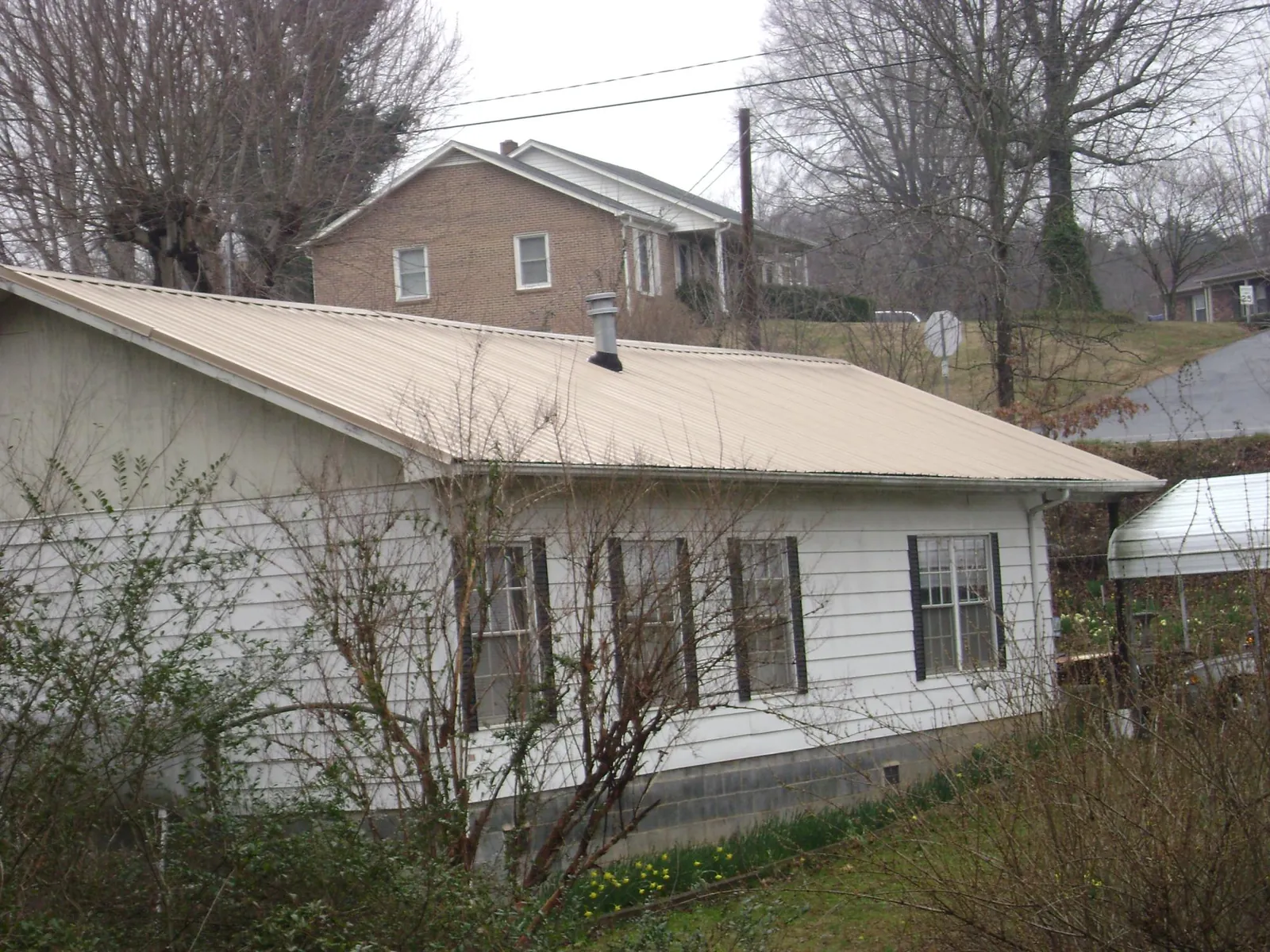 Tan metal roof on a white sided house set into a hillside — Commercial Roofing by Roofing Brothers in Iowa Falls