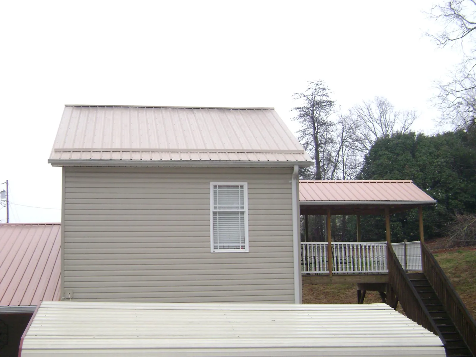 Tan metal roofs on a two story addition and attached porch, from a Roof Replacement job in Iowa Falls